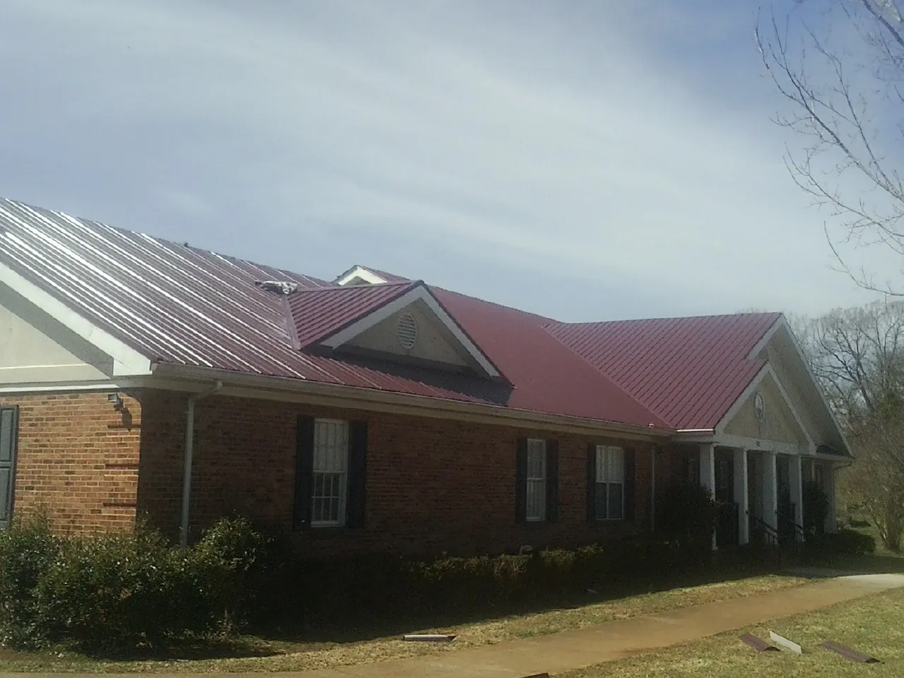 Red metal roof with gabled entries on a long brick building, from a Hail Damage Roof Repair job in Arlington Heights