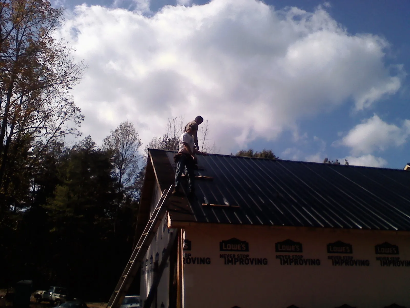 Roofer fastening dark metal panels high against a cloudy sky, from a Roof Inspection job in Arlington Heights