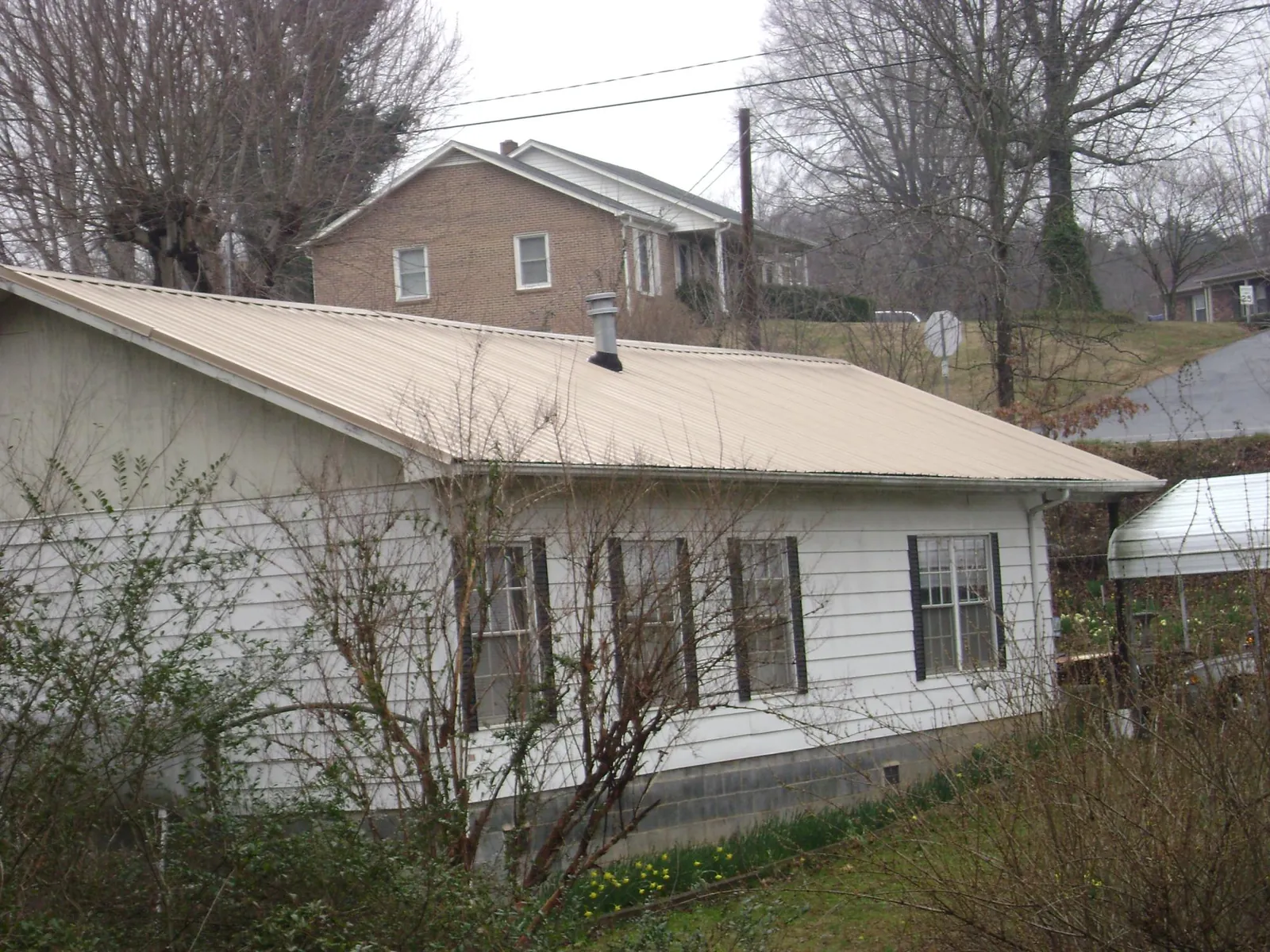 Tan metal roof on a white sided house set into a hillside — Commercial Roofing by Roofing Brothers in Arlington Heights